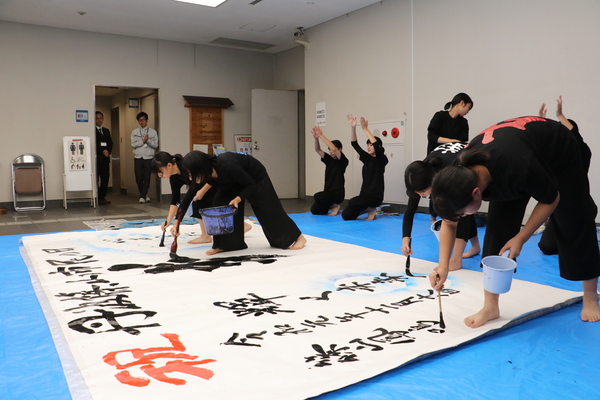 篠山鳳鳴高校書道部部員が筆をもち床面に広げられた大きな白い紙に字を書いている様子