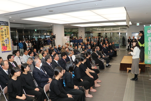 市民ホールにて舞台でマイクをもって話す男性と椅子に座り話をきいている大勢の観客の様子