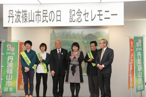 丹波篠山市民の日記念セレモニーと書かれたプレートの下でふるさと大使の方々と、市長、畑さん、梶原さんが並ばれている様子