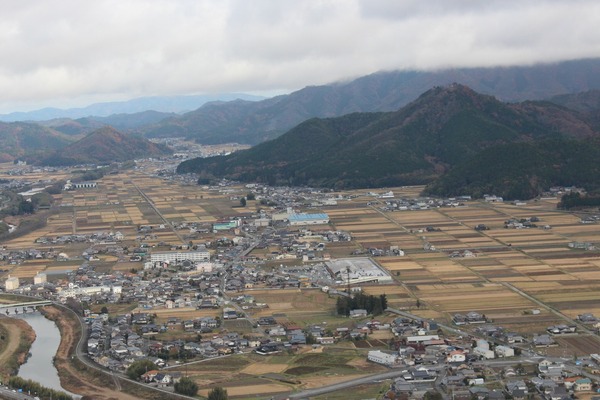 川が流れ点在する建物や田畑がひろがる田園風景の奥に大きな山々がそびえる写真