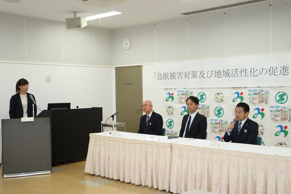 鳥獣被害対策及び地域活性化の促進に関すると書かれたパネルの前で椅子に座り、一名マイクを持ち話す男性と、質問する司会者の女性