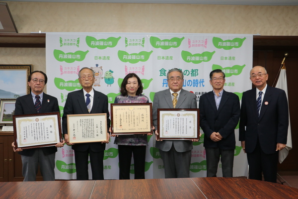 丹波篠山市と書かれた壁の前で、それぞれ賞状をもち立つ表彰者の方々と市長