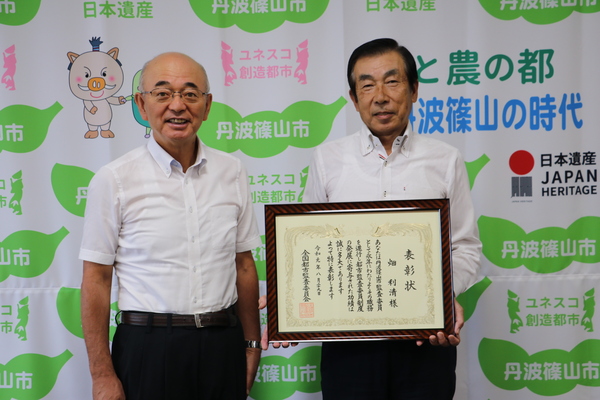 篠山市と書いた壁の前で市長と表彰状をもった畑さんが並んで立っている写真