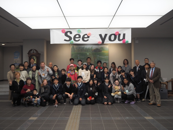 市民ホールにて、またねと英語で書かれたパネルの下で笑顔で並ぶワラワラ市の方々と市長、市職員の写真