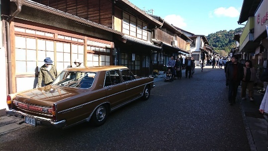 通りに立ち並ぶ伝統的な建築群と通りを歩く人々と、建物前に止められたレトロな車の写真