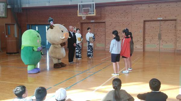 体育館でまるいの、まめりん、市長、市職員が小学生三人と話している様子とそれを見守る小学生の写真