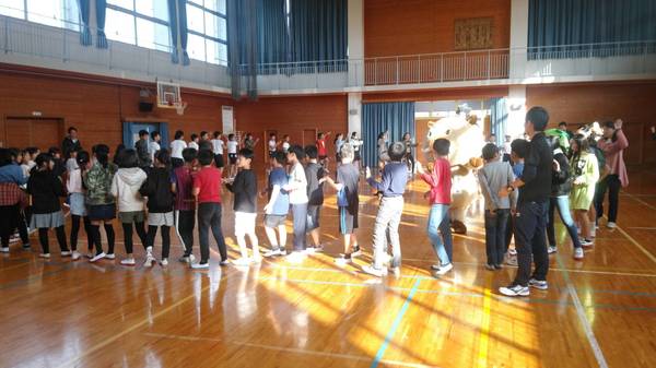 体育館でまるいの、まめりんを囲むように小学生は輪になりデカンショを踊っている様子