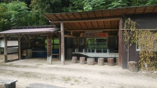青空サロン市場と書かれた看板と木造の建物のなかに木の椅子と机がおいてある写真