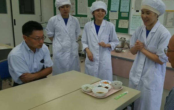 給食メニュー一人分を前に女性職員が説明している様子の写真