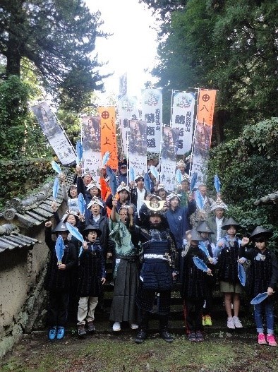 旗をもちながらこぶしをあげオーっと言っている子どもたちと大人が並んでいる写真