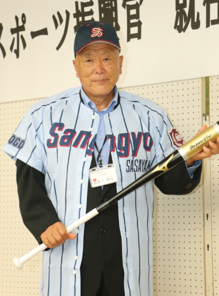 篠山産業高校野球部のユニフォームを羽織った長澤氏がバットを持って記念撮影