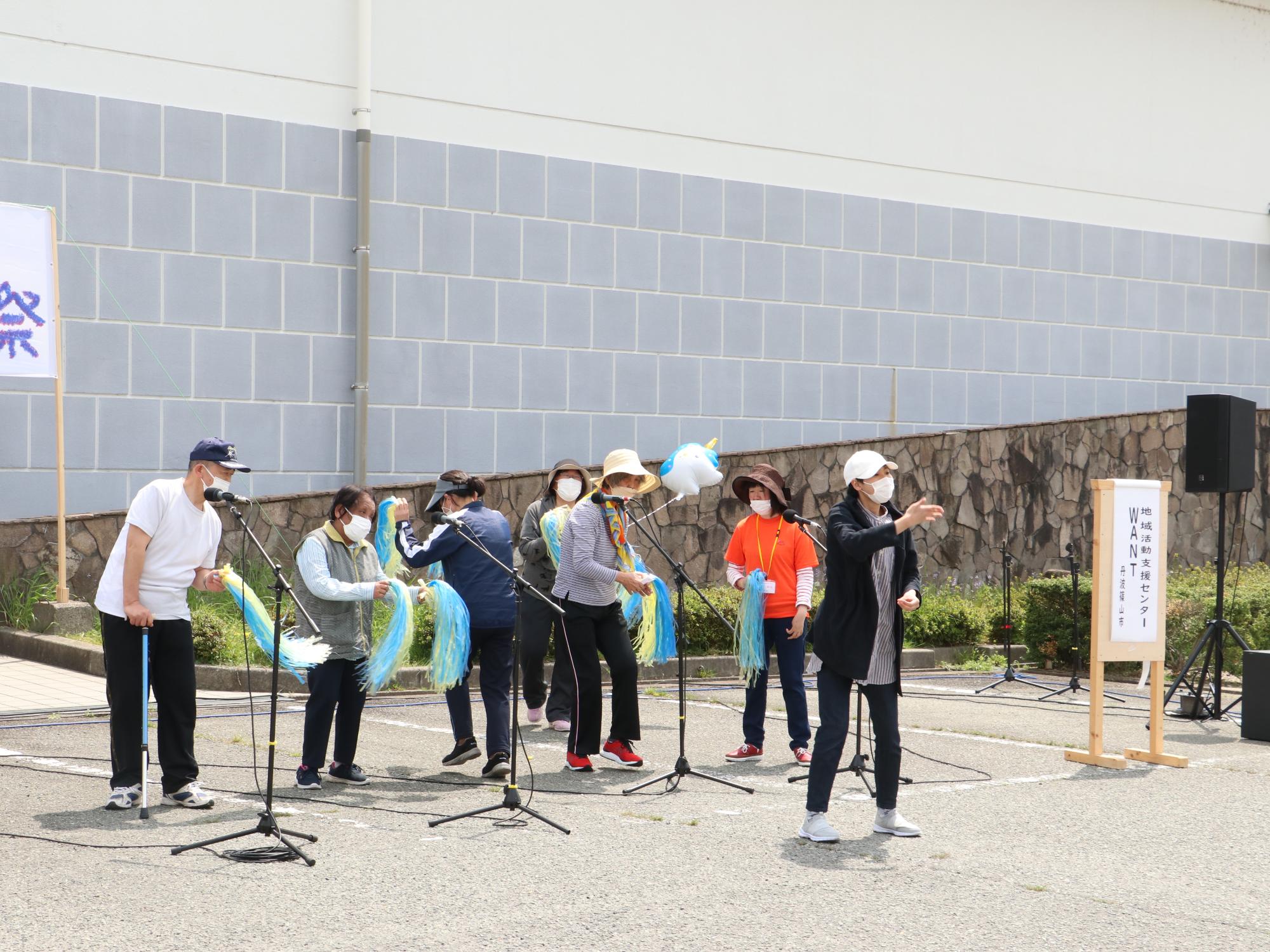 細長い水色と黄色のポンポンを持って発表している