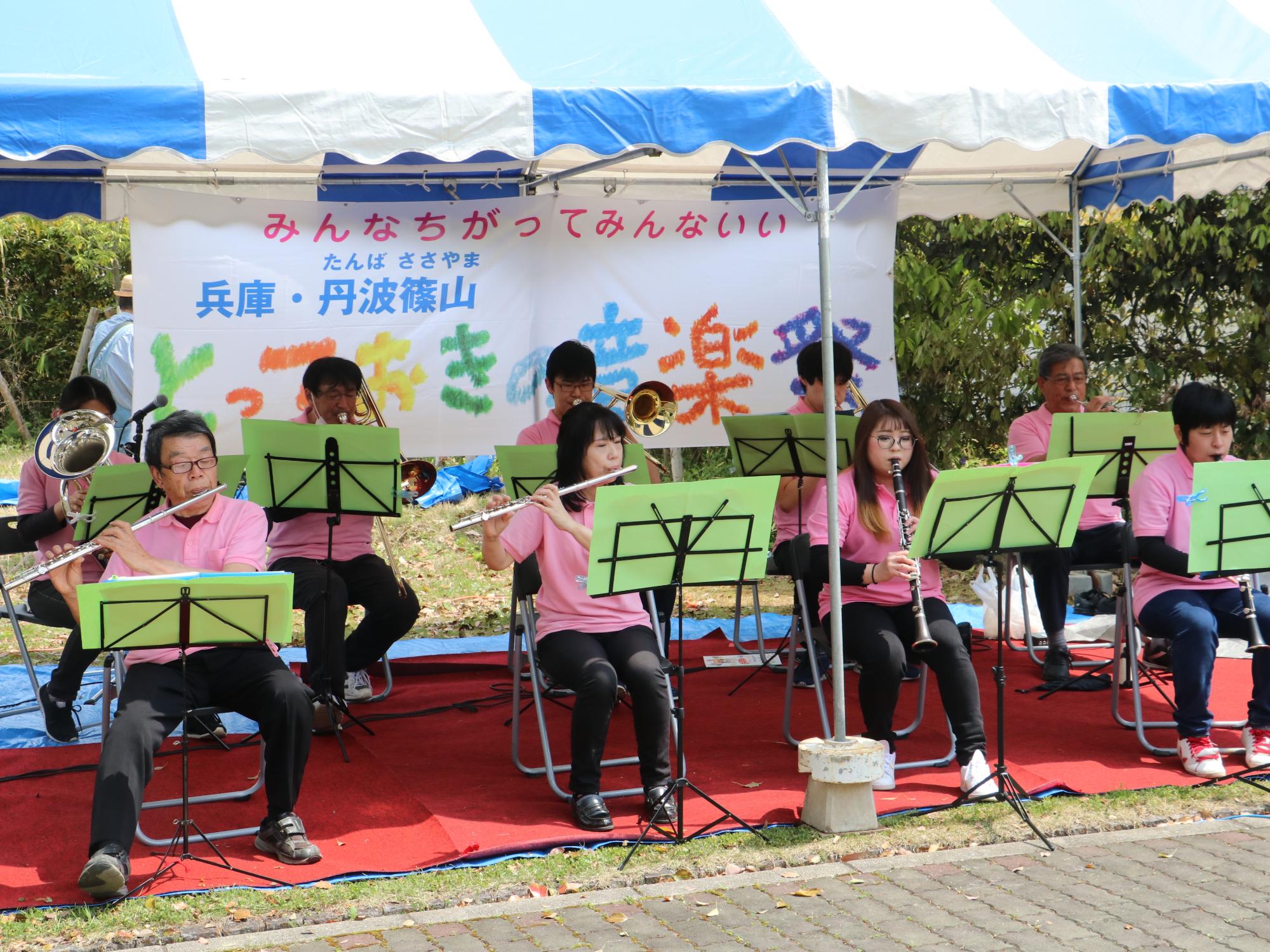 ピンク色のおそろいのポロシャツを着て、フルートやクラリネット、トロンボーンなどを吹いている