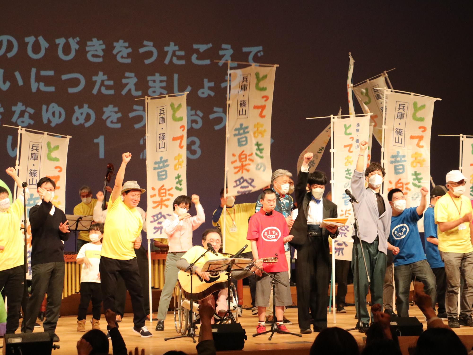 ホールの舞台で、小西実行委員長を中心にとっておきの音楽祭の旗を持ったり演奏している
