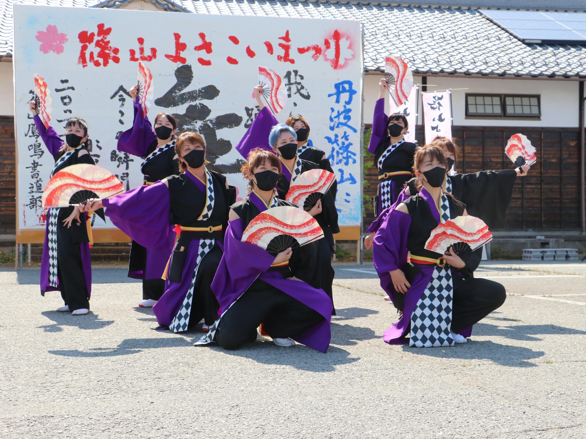 紫の衣装を着て扇子を持って踊っている