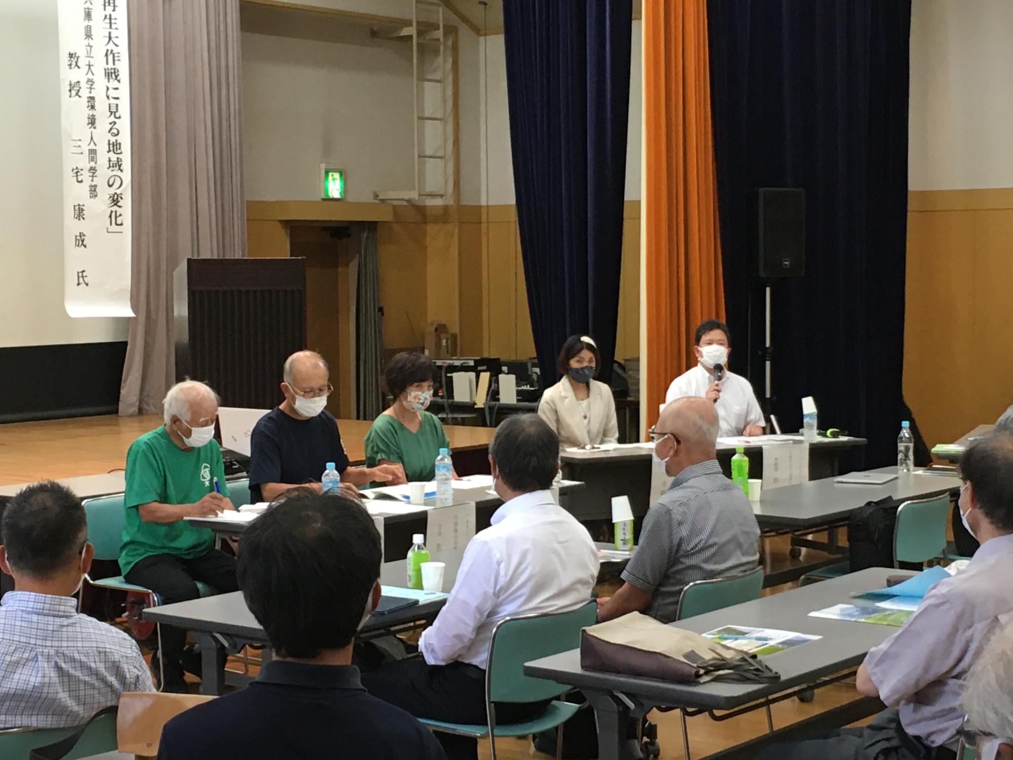 シンポジウムで、前方でパネルトークをしている。