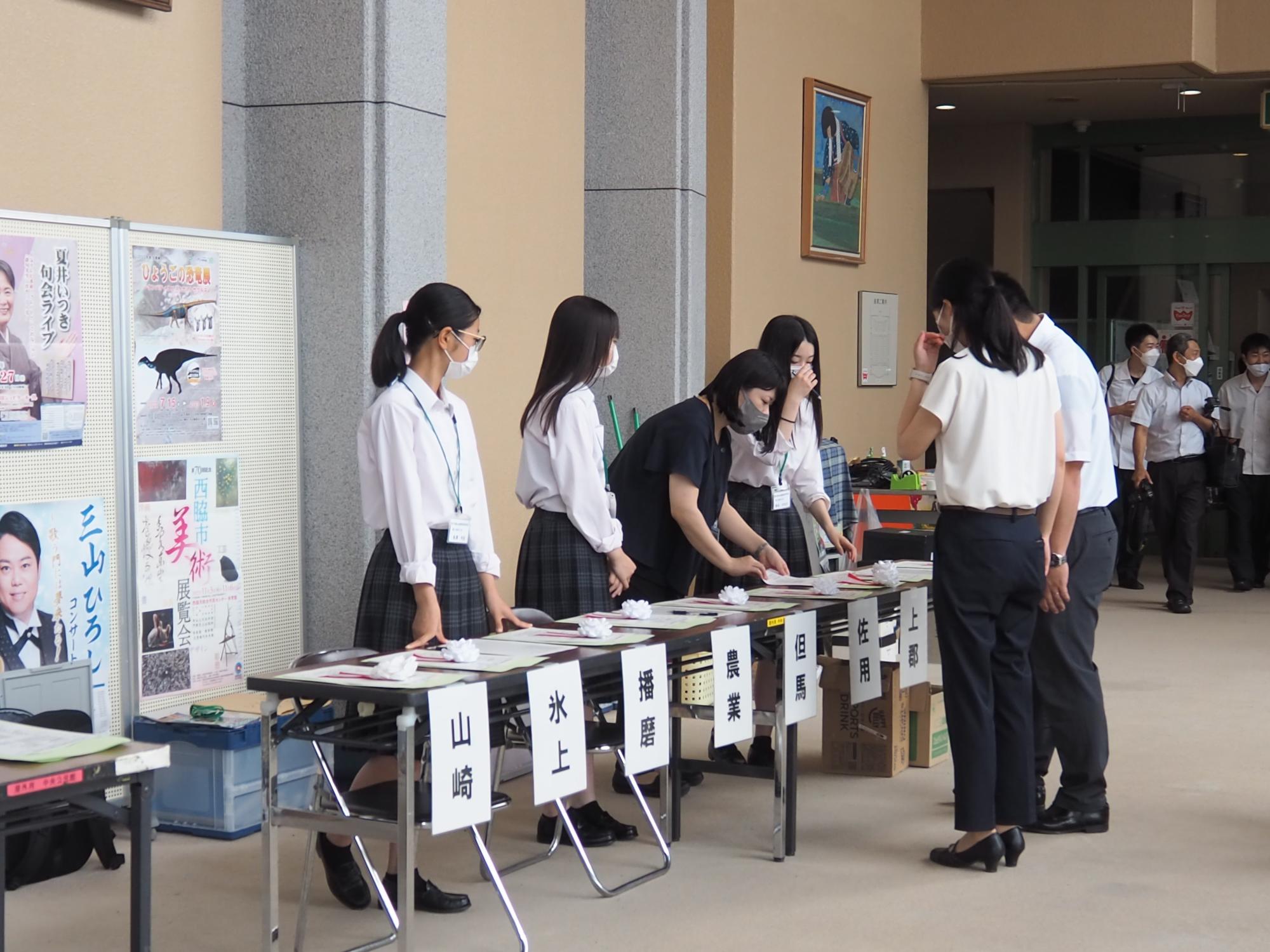 ホール前で、机に各高校名を貼って学生たちが受付を行っている。