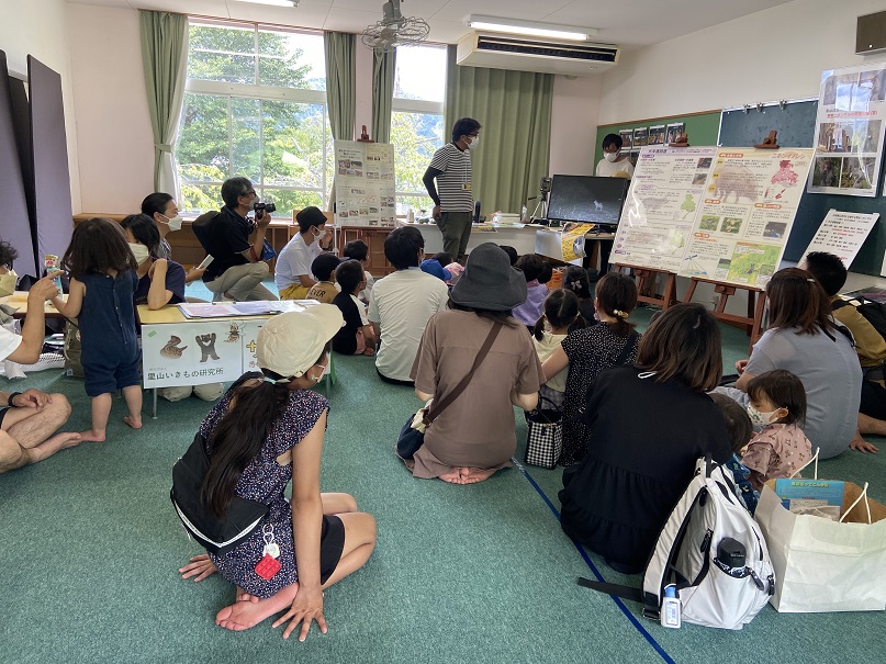 室内で大きな模造紙に生き物や環境の発表をたくさんの親子連れが座って聞いている