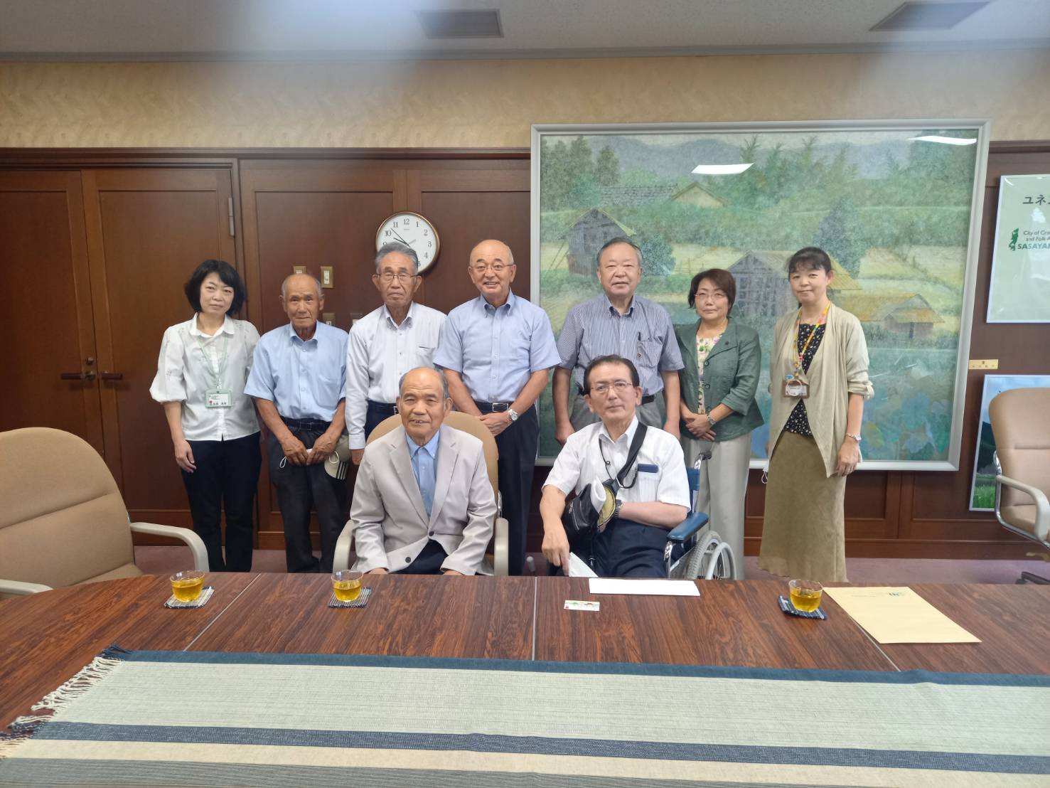 前列に男性二人が座っていて、後列に市長や市職員、市議会議員が立っている