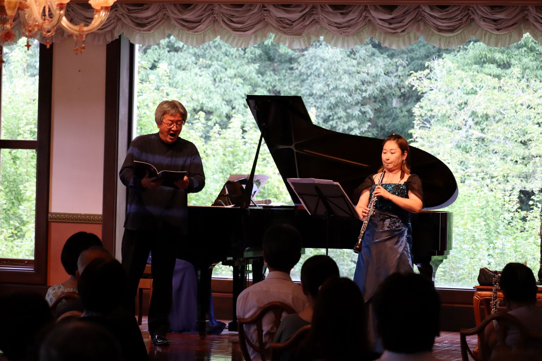 ピアノの前で女性がオーボエを演奏しており、男性が歌っている
