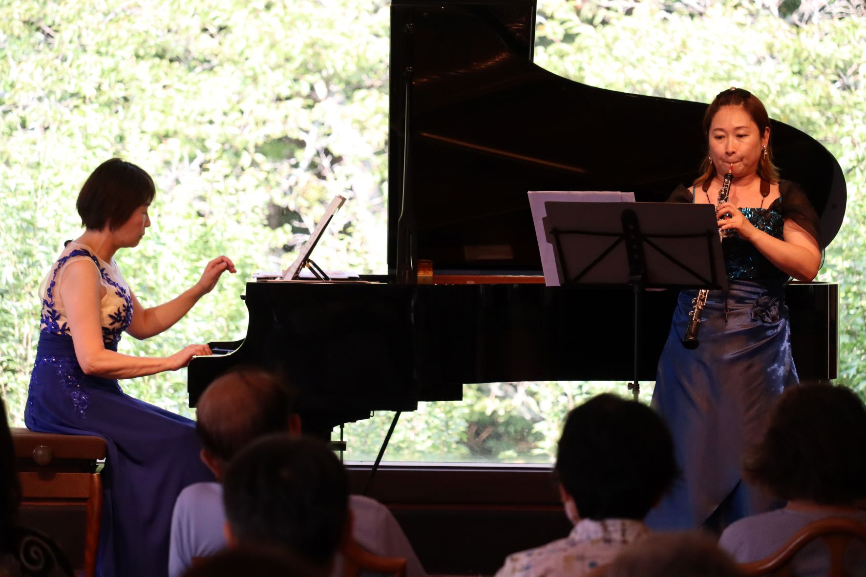 女性がピアノを演奏し、その前で女性がオーボエを演奏している。