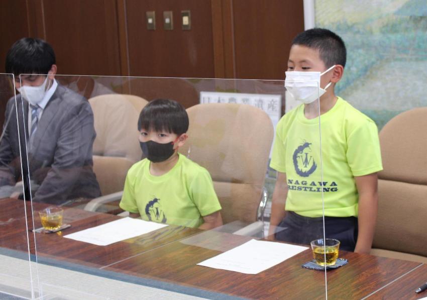 表敬訪問で、レスリングチームのTシャツを着た男の子が立ってお話している。