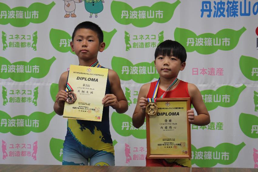 レスリングのユニフォームを着た男の子人が、メダルを首からさげて表彰状を手に持っている