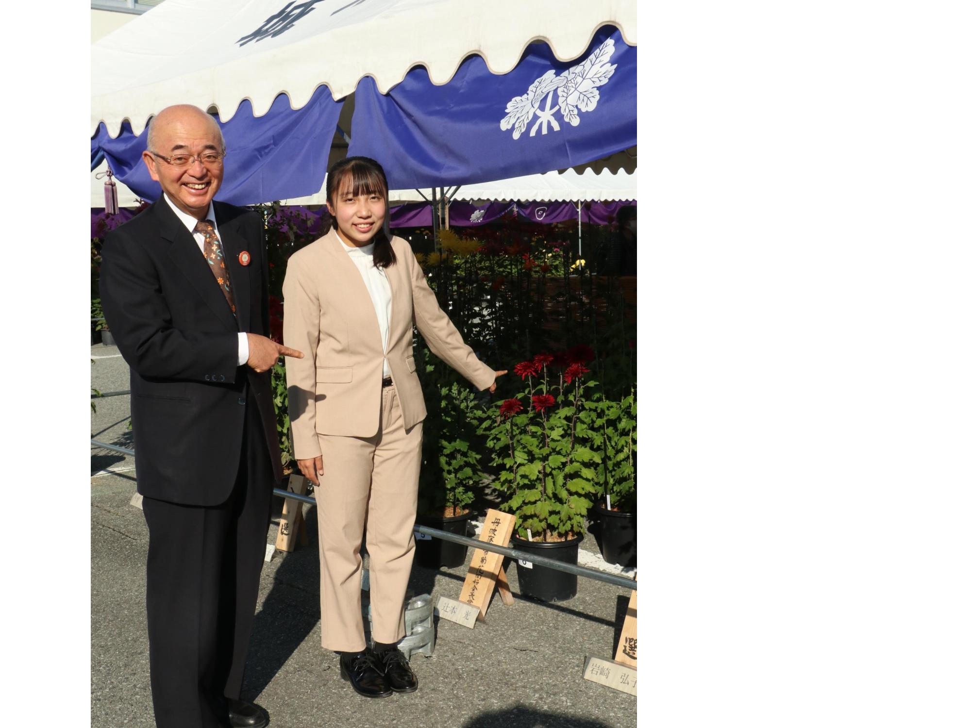 市長と受賞者が受賞作品の菊を指さしている