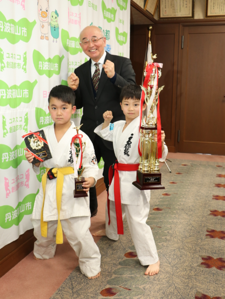 男の子2人がトロフィーを持って、市長と記念撮影