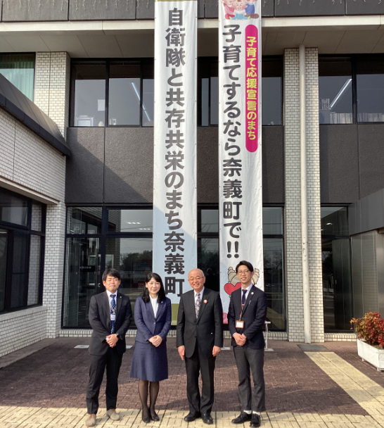 子育てするなら奈義町でという懸垂幕の前で、市長の市職員が記念撮影