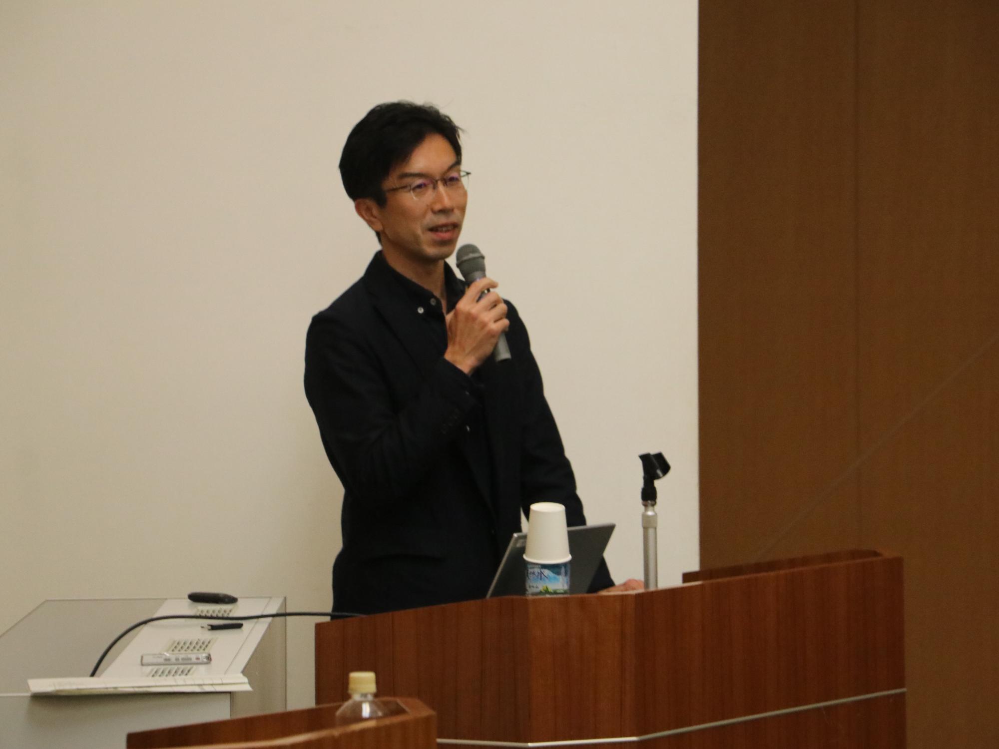 マイクを持って講演をする西成教授