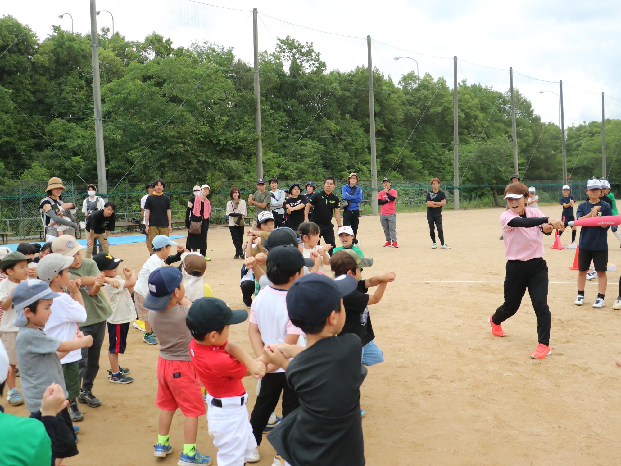 バットの振り方を教える宇津木さんとバットを振る練習をする子どもたち