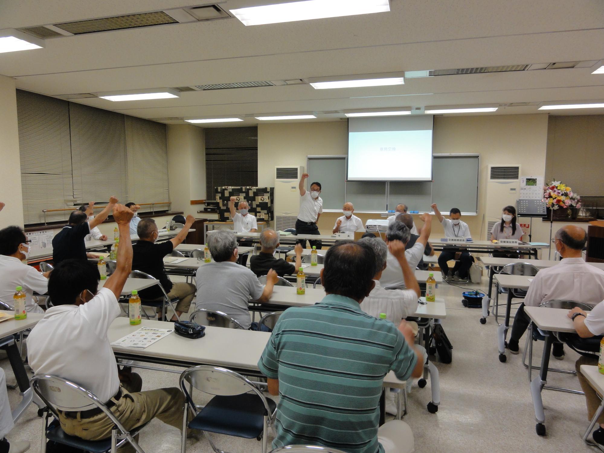 会議の最後に、参加者全員でこぶしを出して「ガンバロー」と言っている