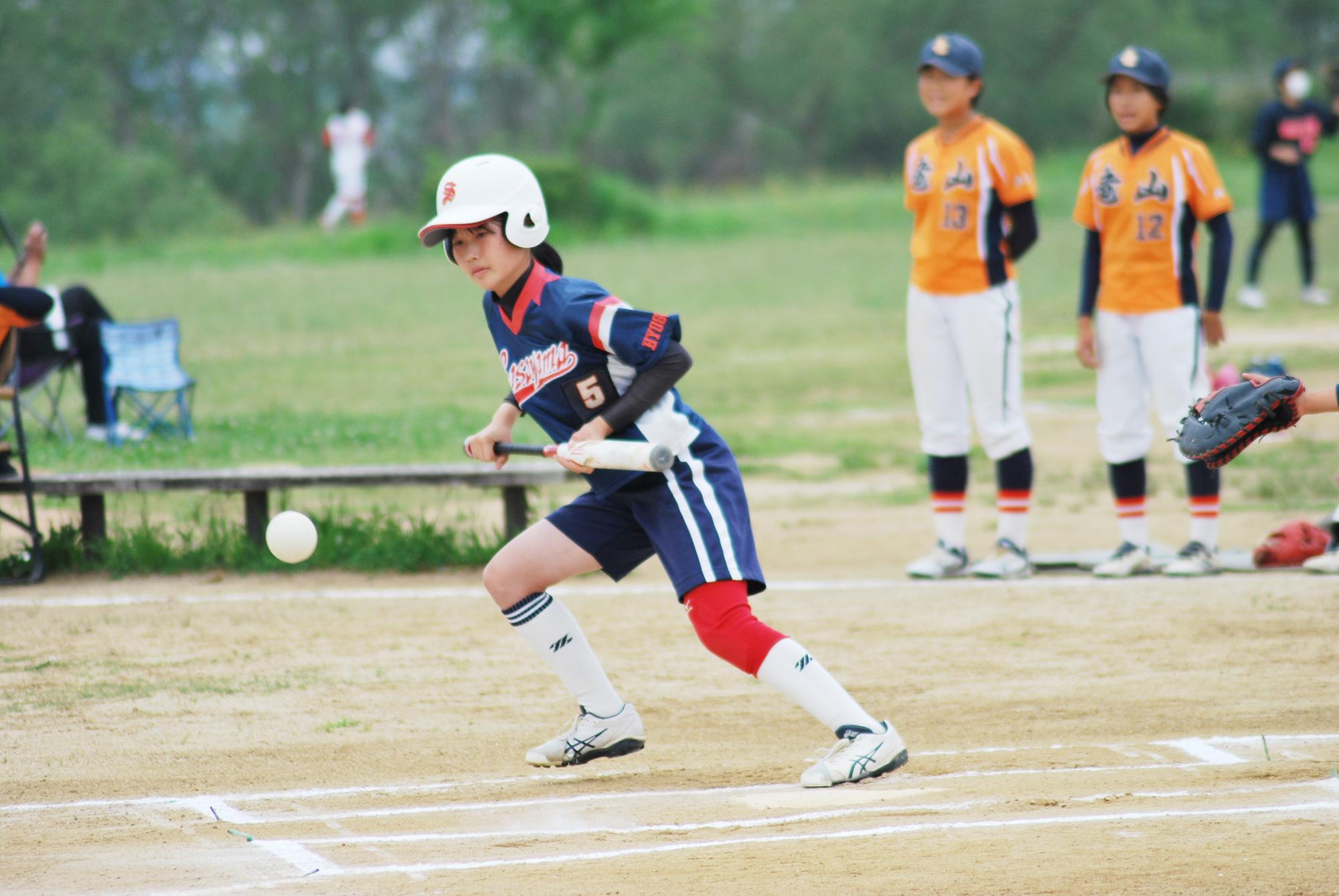 ソフトボールのユニフォームを着た女の子がバントをしている