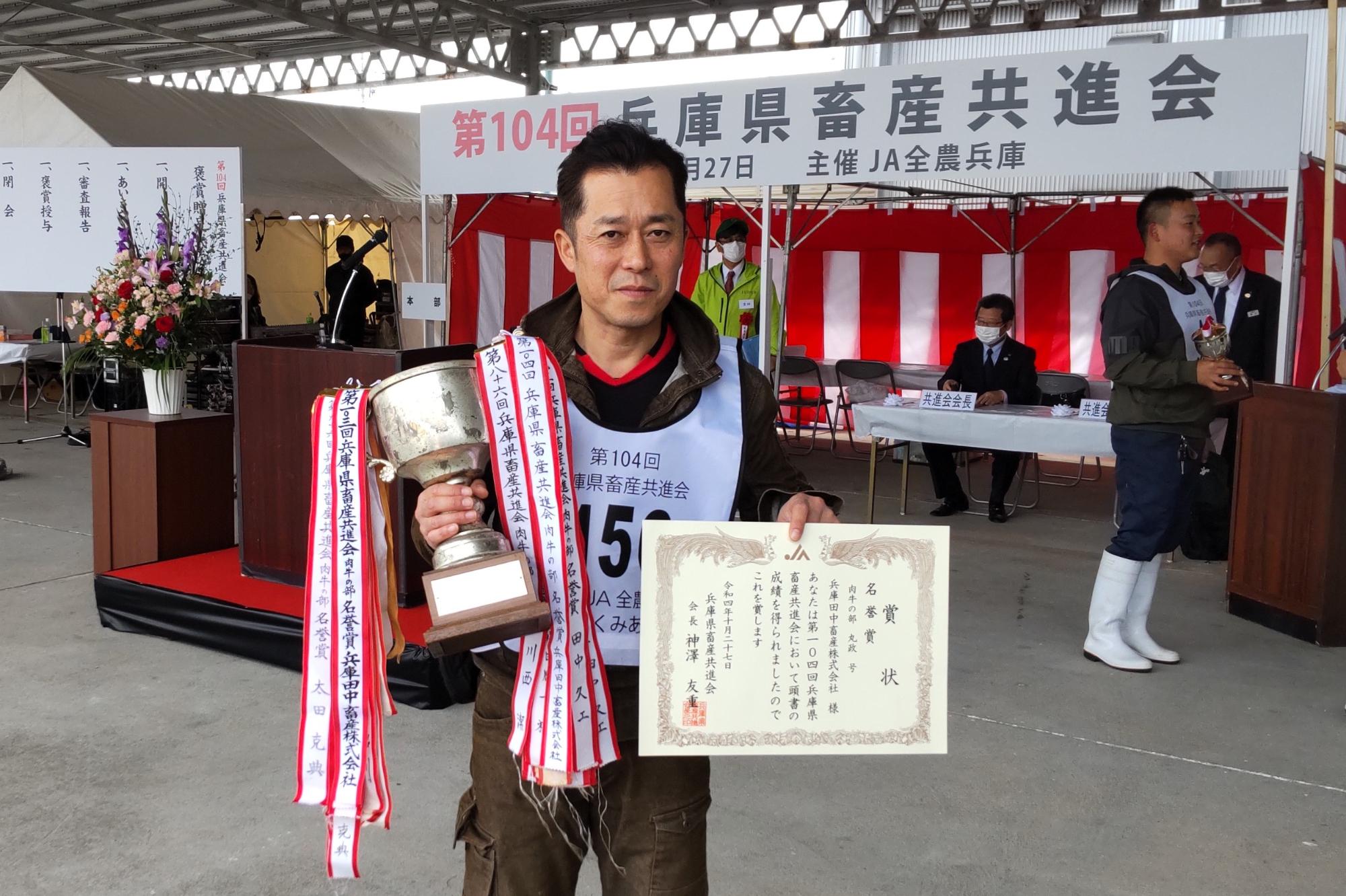 表彰状とトロフィーを手に持っている田中さん