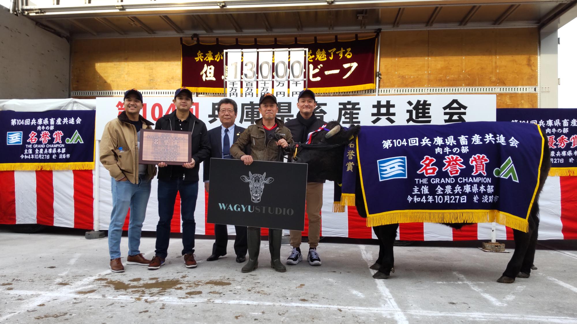 1300万円で落札の前で、名誉賞の横断幕を牛にかけ、関係者が記念撮影している