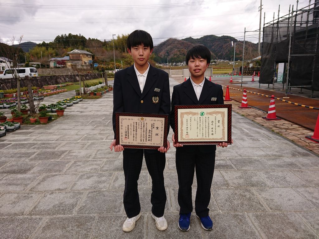 税の作文で表彰を受けた2人の生徒が表彰状を持って並んでいる