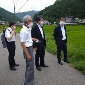 スーツを着た男性2人に、地元の男性がほ場のことを説明している