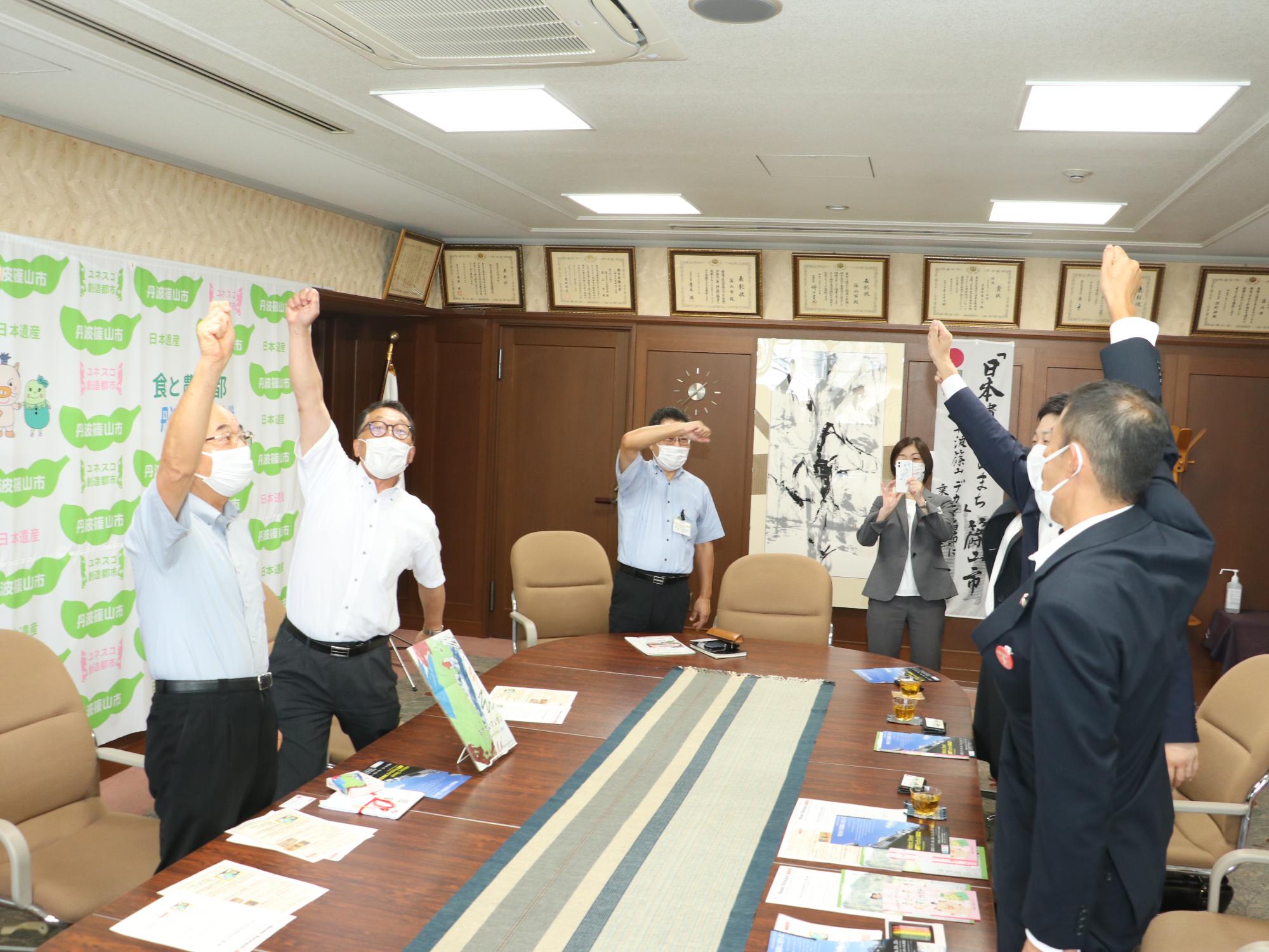 市長、教育長、おやさいクレヨンを寄贈していただいた会社の方がオーと手をあげている。