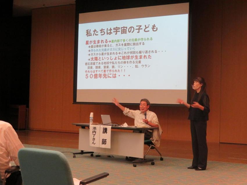 スライドを使って講師の先生がお話をされている。そばには手話通訳者の女性が立っている。