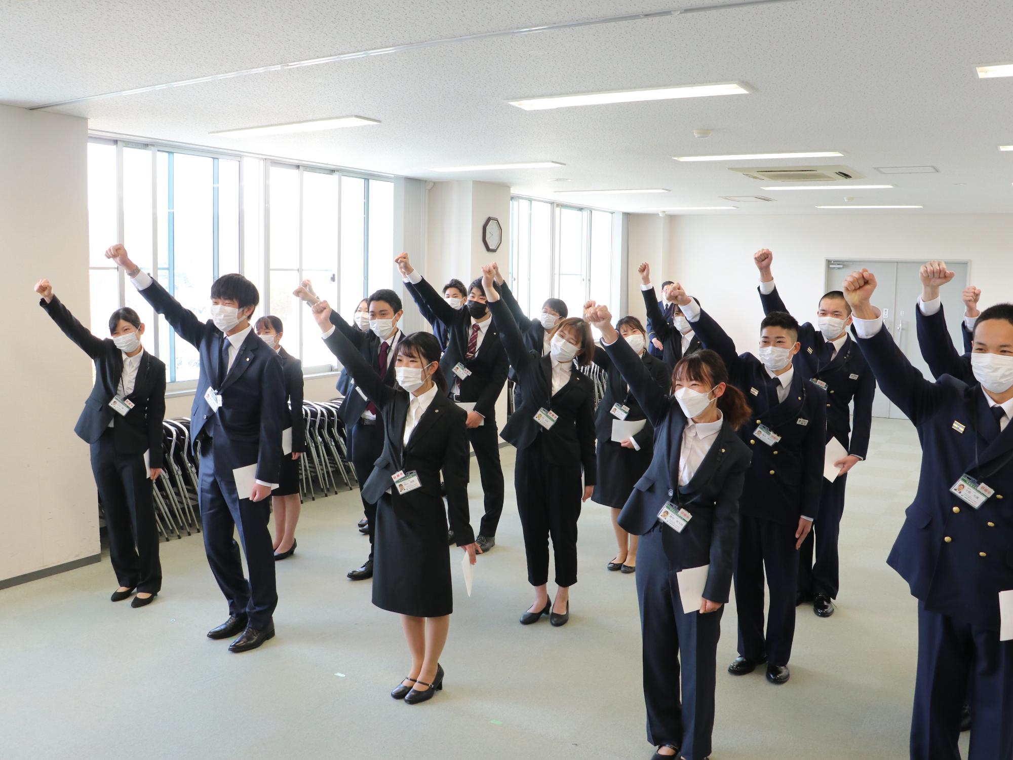辞令を受け取った新規採用職員が18名が右手のこぶしをにぎってあげている
