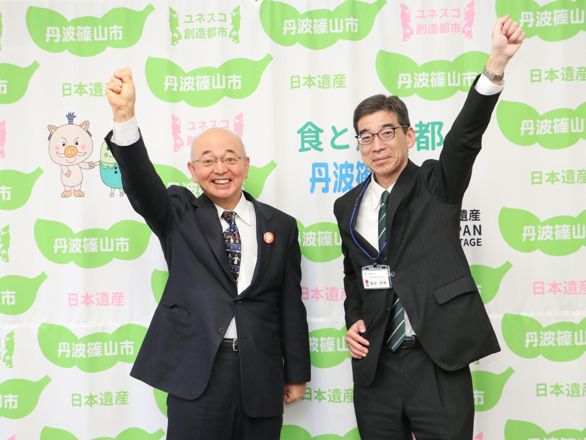 市長と観光政策官がこぶしをにぎってあげている