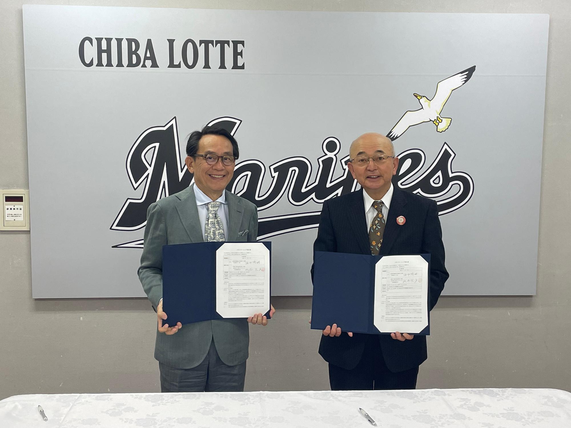 千葉ロッテマリーンズと書かれたパネルの前で、市長と球団社長が契約書を手に持っている