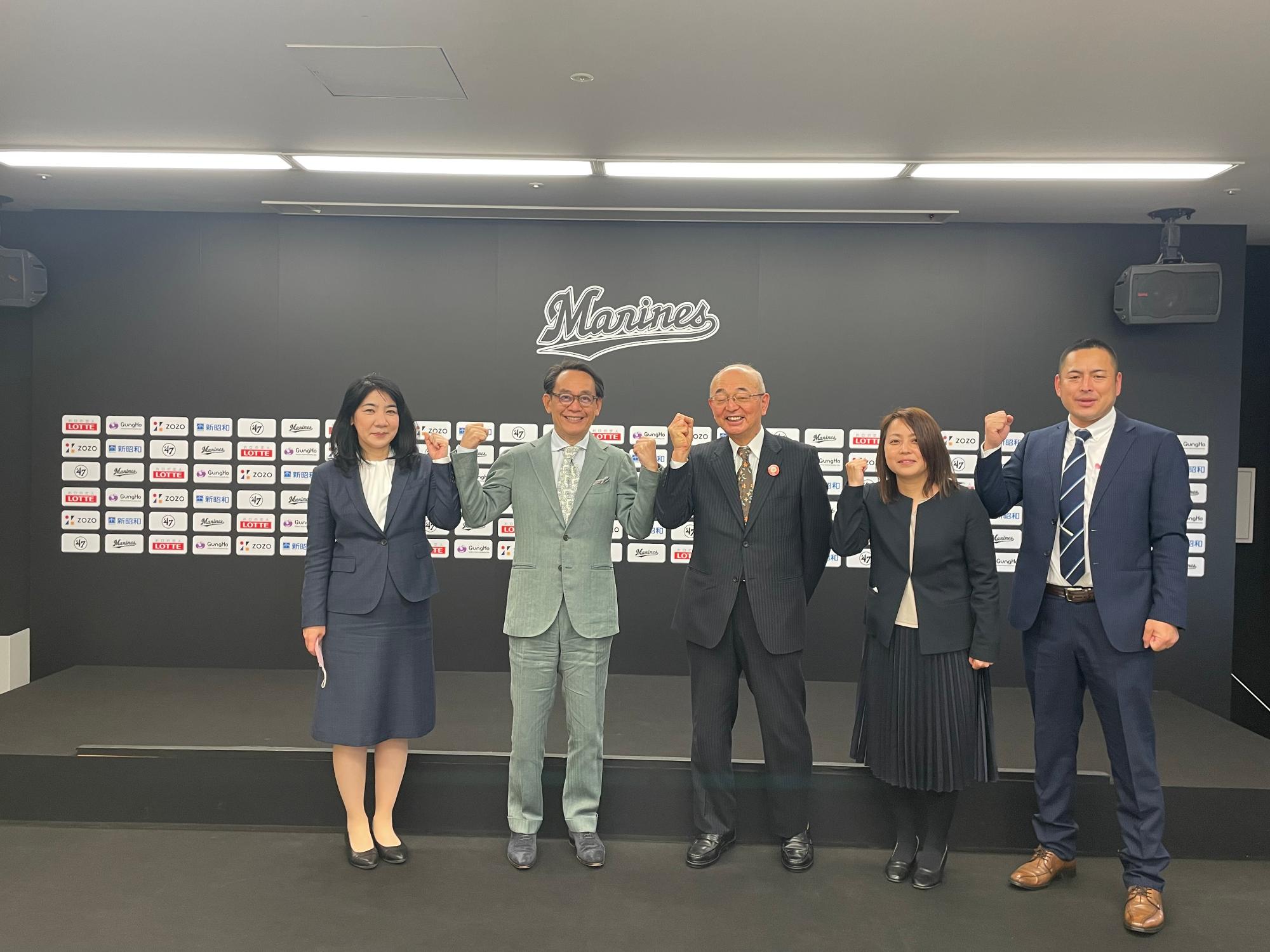 球団社長と市長を真ん中に、その両隣に市職員が並んでガッツポーズをしている