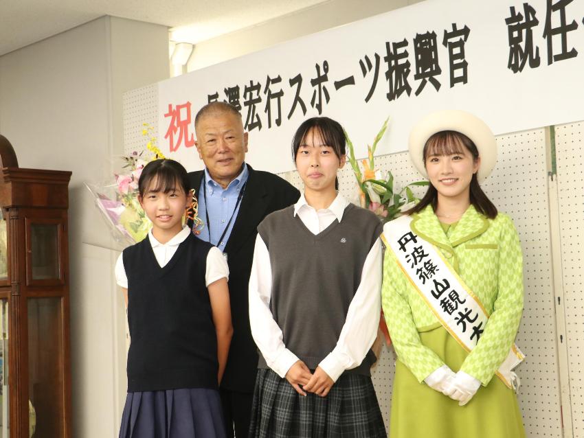 長澤先生が観光大使、野球部マネージャー、ソフトボールチームの女の子から花束を受け取り、記念撮影をしている