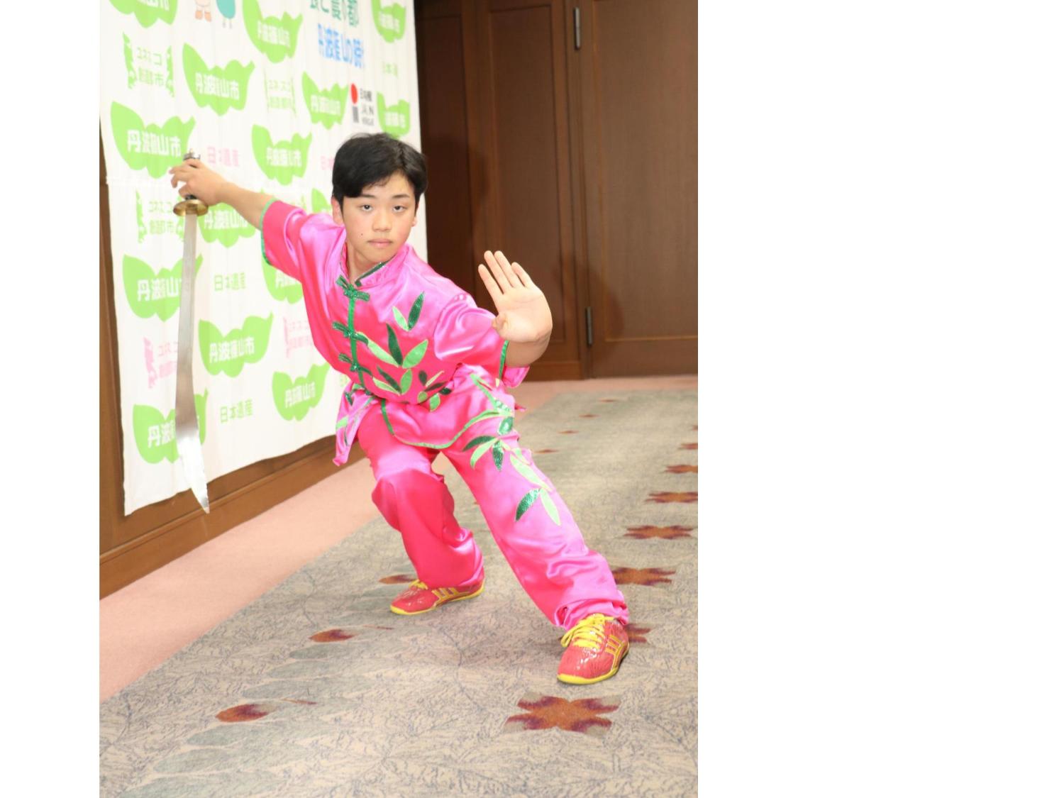 ピンク色の衣装を着た男の子が剣を持って太極拳の演舞を披露している