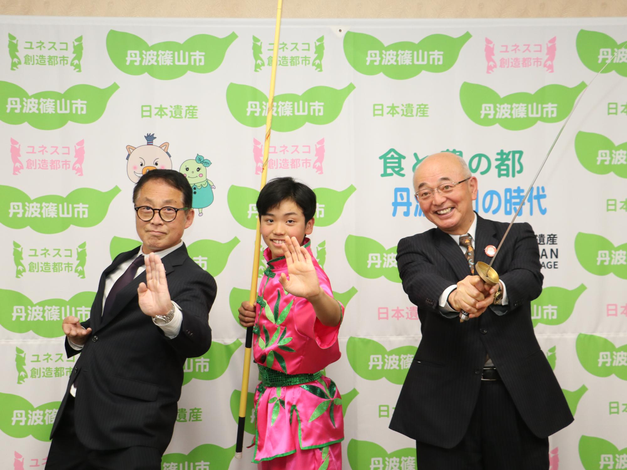 ピンク色の衣装を着た男の子と市長、教育長がそれぞれ太極拳のポーズをとっている