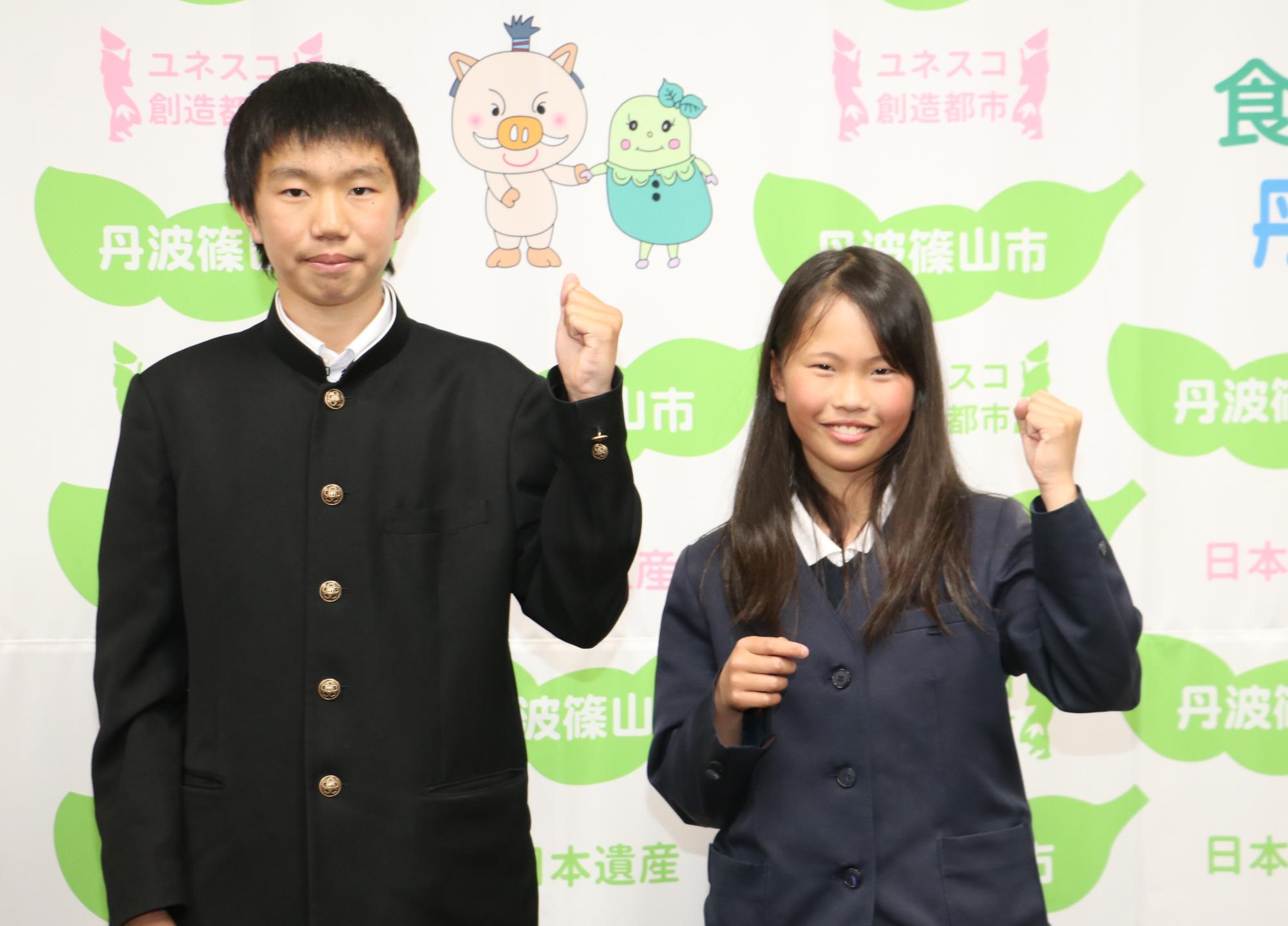 兄妹で、まるいのまめりんのタペストリーの前でガッツポーズしている