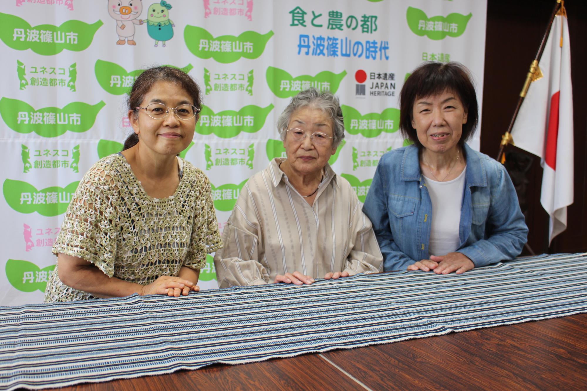 テーブルに、丹波木綿のテーブルセンターを広げて、製作された女性3人の記念撮影
