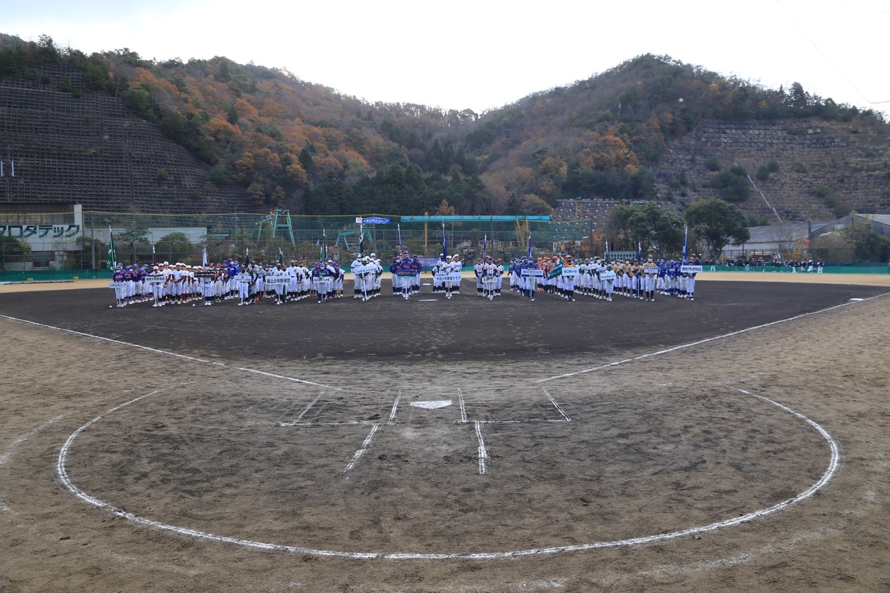 グラウンドで、野球大会に出場するチームが並んで入場行進している。